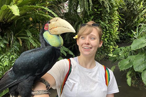 Photo of a 波胆网站 student in a jungle with a large exotic bird perched on her arm