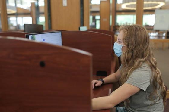 Photo of a female Chatham University 学生 wearing a mask, working on a computer in the library
